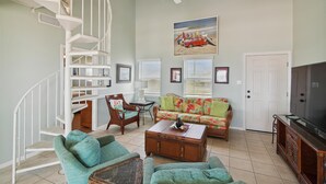 A living room with a spiral staircase, a sofa, two armchairs, a coffee table, and a television. - Sea Loft by Ryson Vacation Rentals (Galveston)