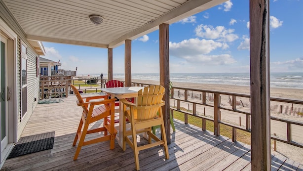 A wooden deck with a table and chairs overlooking a beach. - Sea Loft by Ryson Vacation Rentals (Galveston)