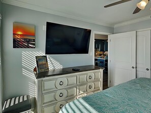 Une chambre à coucher comprenant un lit, une commode, un téléviseur fixé au mur et une porte donnant sur une salle de bain.