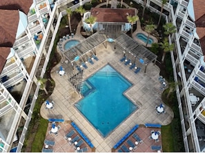 Vista aérea de um hotel com piscina central rodeada por áreas de descanso e várias varandas.