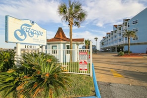 A resort rental sign with a palm tree and a gated parking area. - Beachcomber by Ryson Vacation Rentals (Galveston)