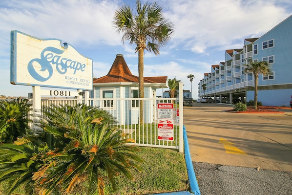 A resort rental sign with a palm tree and a gated parking area. - Beachcomber by Ryson Vacation Rentals (Galveston)