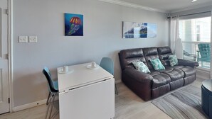 A living room with a brown leather sofa, a white coffee table, and a blue chair. There are two paintings on the wall.