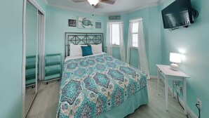 A bedroom with a bed, a ceiling fan, a TV, and a bedside table with a lamp.