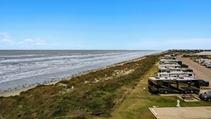 A beachside RV park with rows of RVs parked along the shore, a sandy beach, and the ocean in the background.