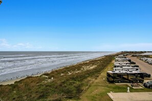 Ein Wohnmobilpark direkt am Strand mit Reihen von Wohnmobilen, die entlang der Küste geparkt sind, einem Sandstrand und dem Meer im Hintergrund.
