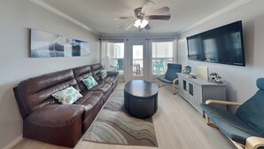 A living room with a brown leather sofa, a round coffee table, a blue armchair, a TV, and a ceiling fan.
