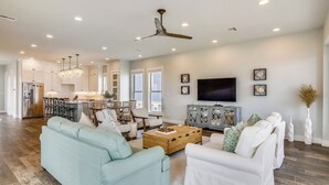 A spacious living room with a light blue sofa, a white sofa, and a wooden coffee table. There is a TV, a cabinet, and a ceiling fan. - Skin and Bones by Ryson Vacation Rentals (Galveston)