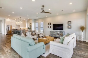 A spacious living room with a light blue sofa, a white sofa, and a wooden coffee table. There is a TV, a cabinet, and a ceiling fan. - Skin and Bones by Ryson Vacation Rentals (Galveston)