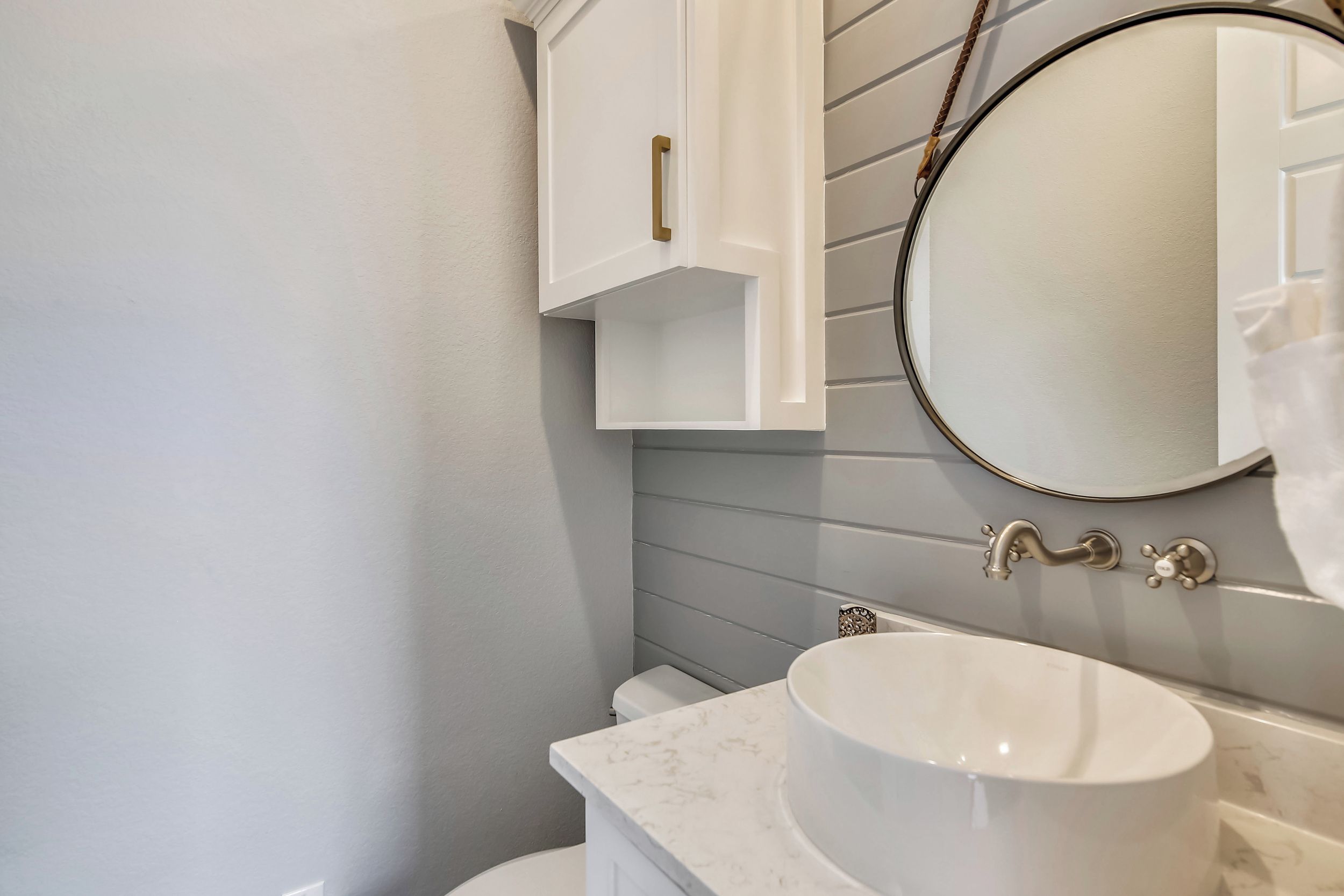 Un baño con un lavamanos blanco, un espejo redondo y un mueble blanco con pomo de latón.