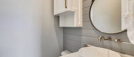 Un baño con un lavamanos blanco, un espejo redondo y un mueble blanco con pomo de latón.