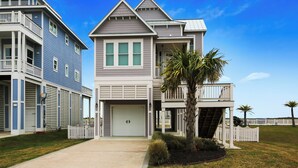 A two-story residential building with a garage, a balcony, and a well-maintained lawn with palm trees. - Skin and Bones by Ryson Vacation Rentals (Galveston)