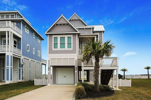 A two-story residential building with a garage, a balcony, and a well-maintained lawn with palm trees. - Skin and Bones by Ryson Vacation Rentals (Galveston)