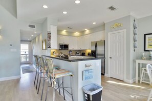 Une cuisine moderne avec des meubles blancs, des appareils en acier inoxydable et un îlot central doté de tabourets de bar.