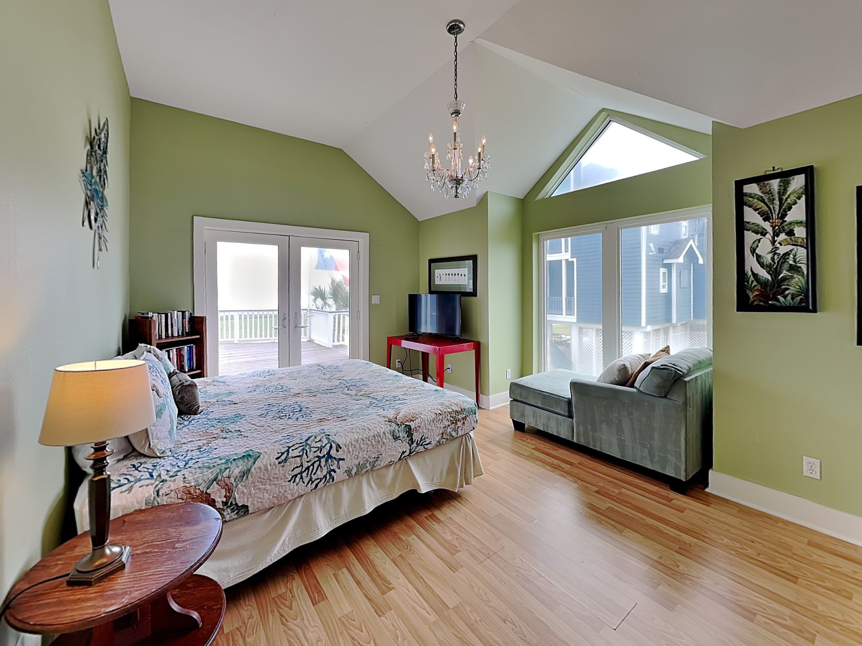 A bedroom with a bed, a desk, a chair, a lamp, and a balcony with a view.