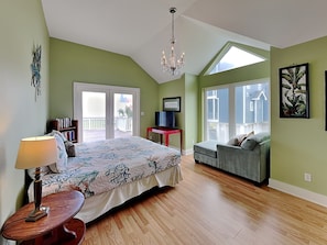 A bedroom with a bed, a desk, a chair, a lamp, and a balcony with a view.