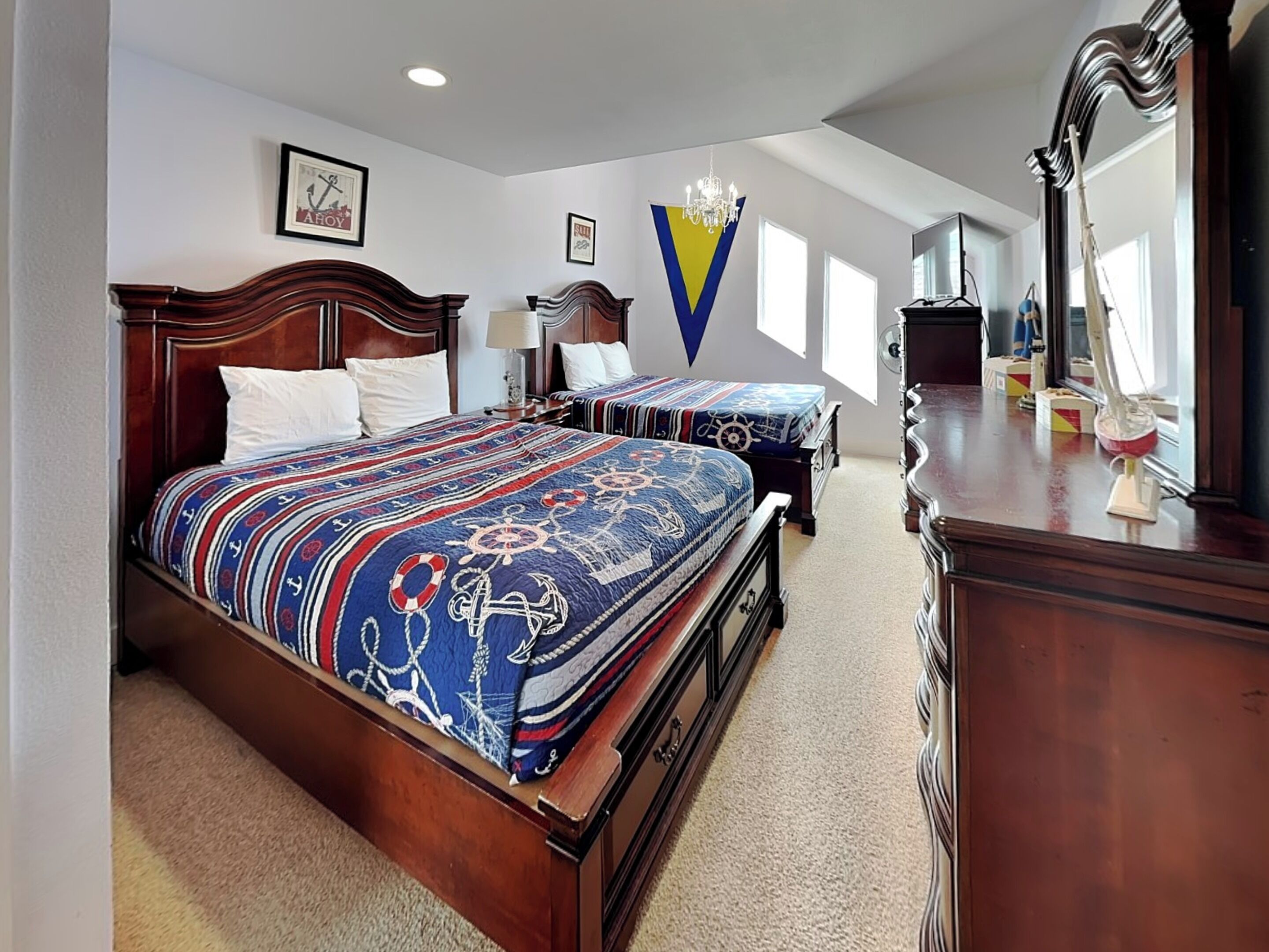 A bedroom with two beds, a dresser, a mirror, and a chandelier.