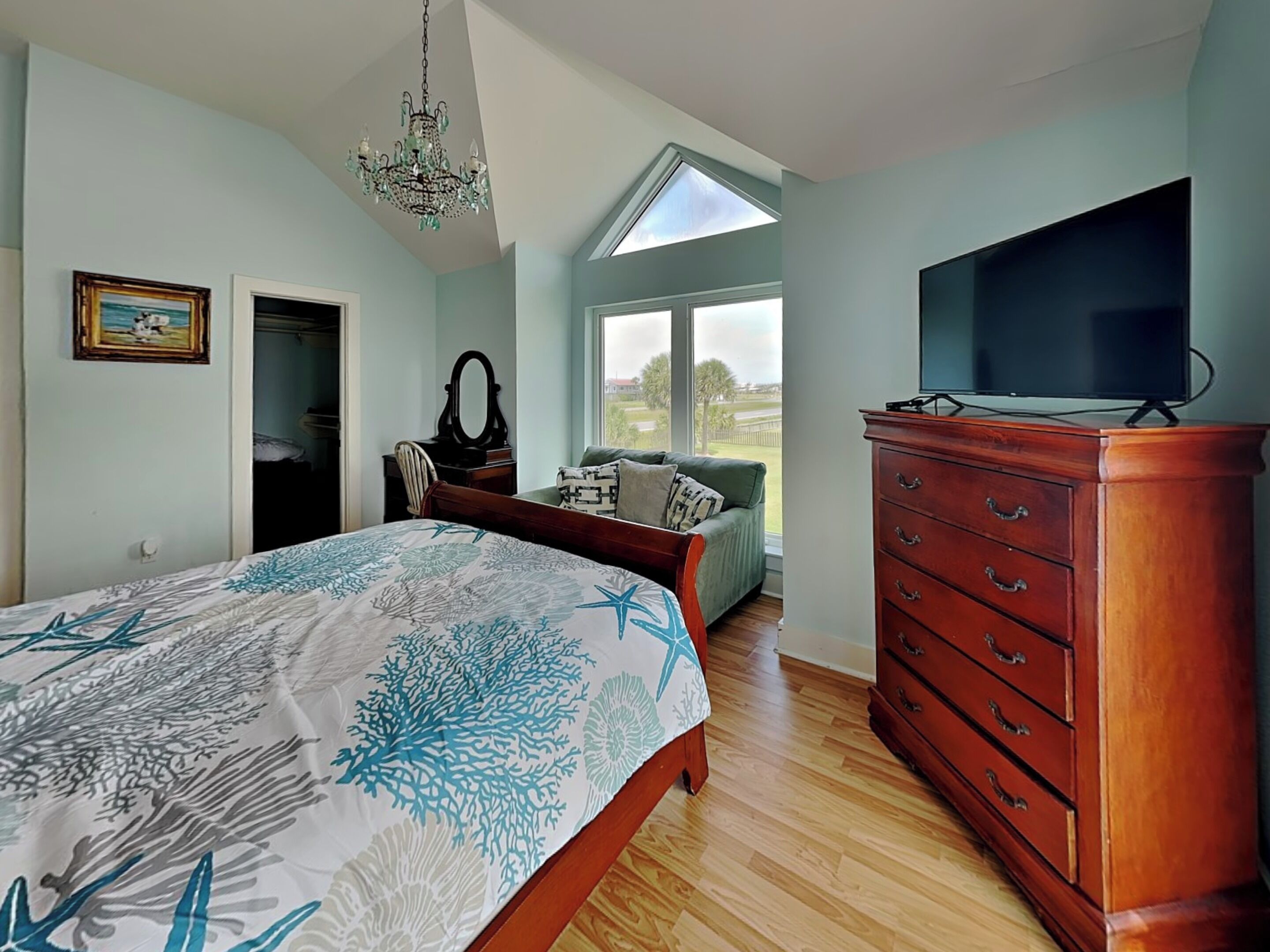 A bedroom with a bed, dresser, TV, and a window with a view.