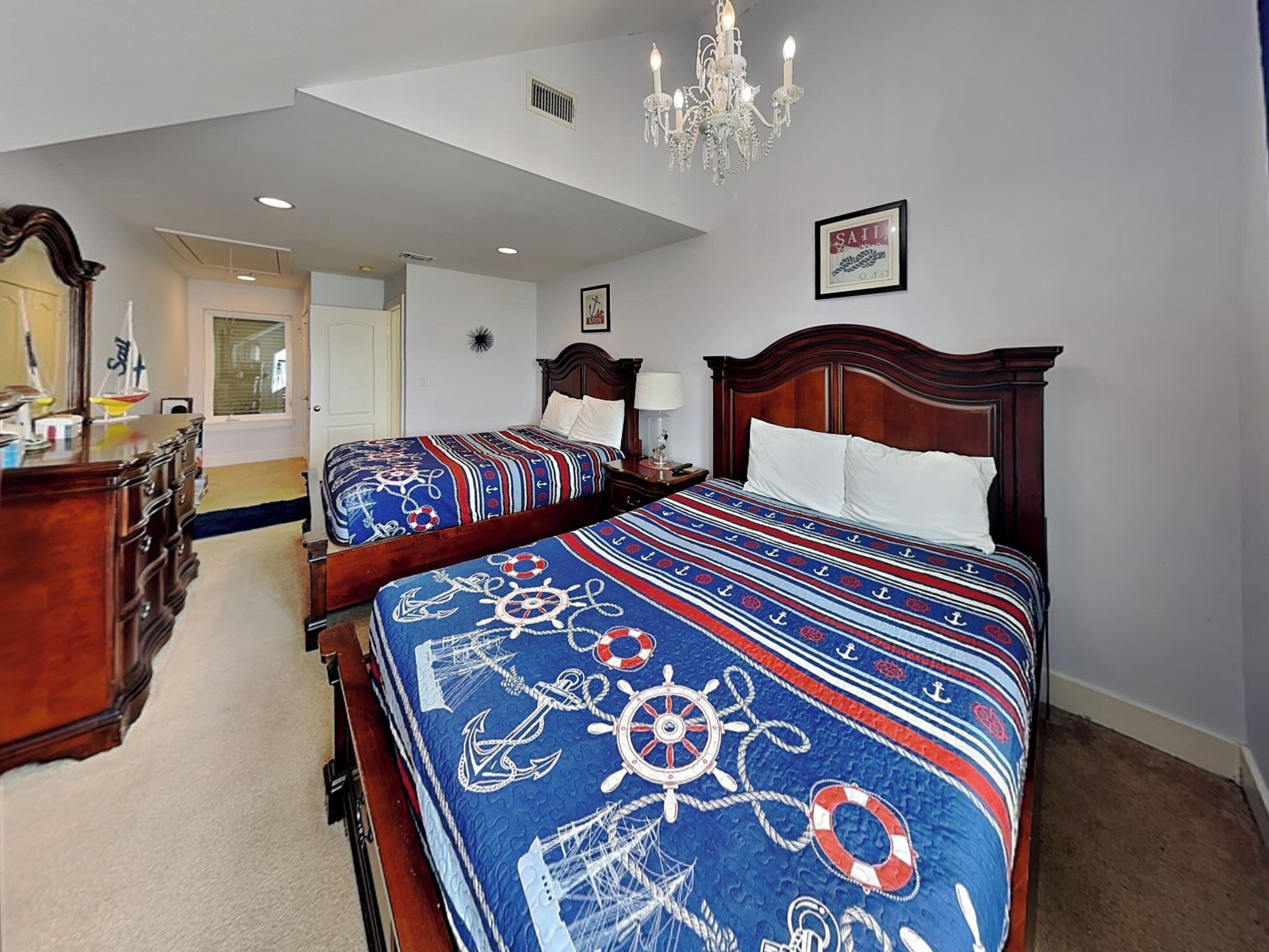 A hotel room with two beds, a chandelier, a framed picture on the wall, and a dresser.