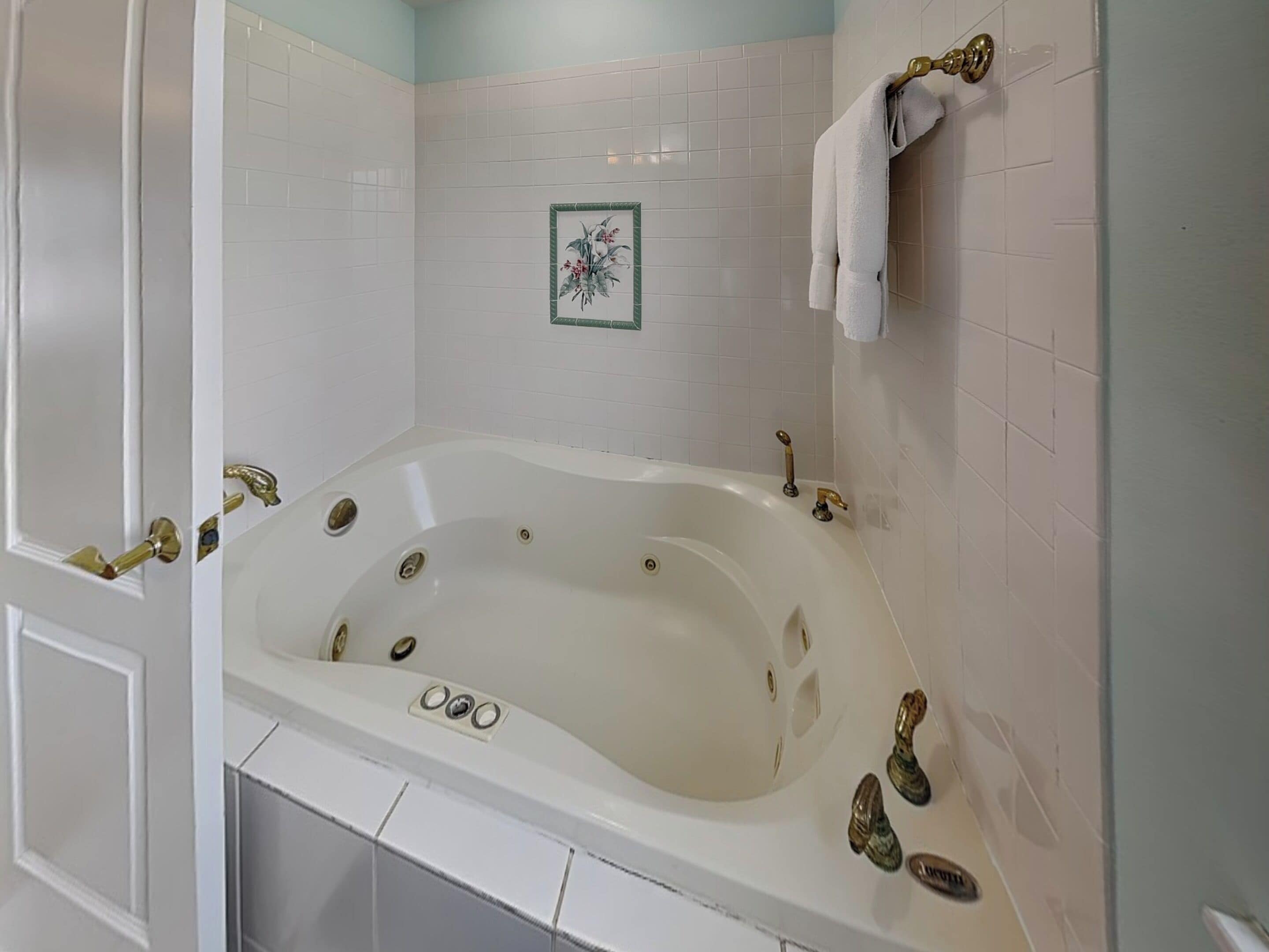 A white bathtub with gold fixtures, white tiled walls, and a small framed picture on the wall.