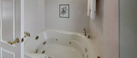 A white bathtub with gold fixtures, white tiled walls, and a small framed picture on the wall.