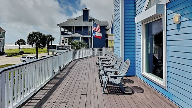 Un pontile in legno con sedie, una ringhiera e un edificio con facciata blu e una bandiera americana.