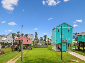 A residential neighborhood with colorful houses, a grassy yard, and a clear blue sky. - Sunny Beach Sandcastle Cottage by Ryson Vacation Rentals (Galveston)
