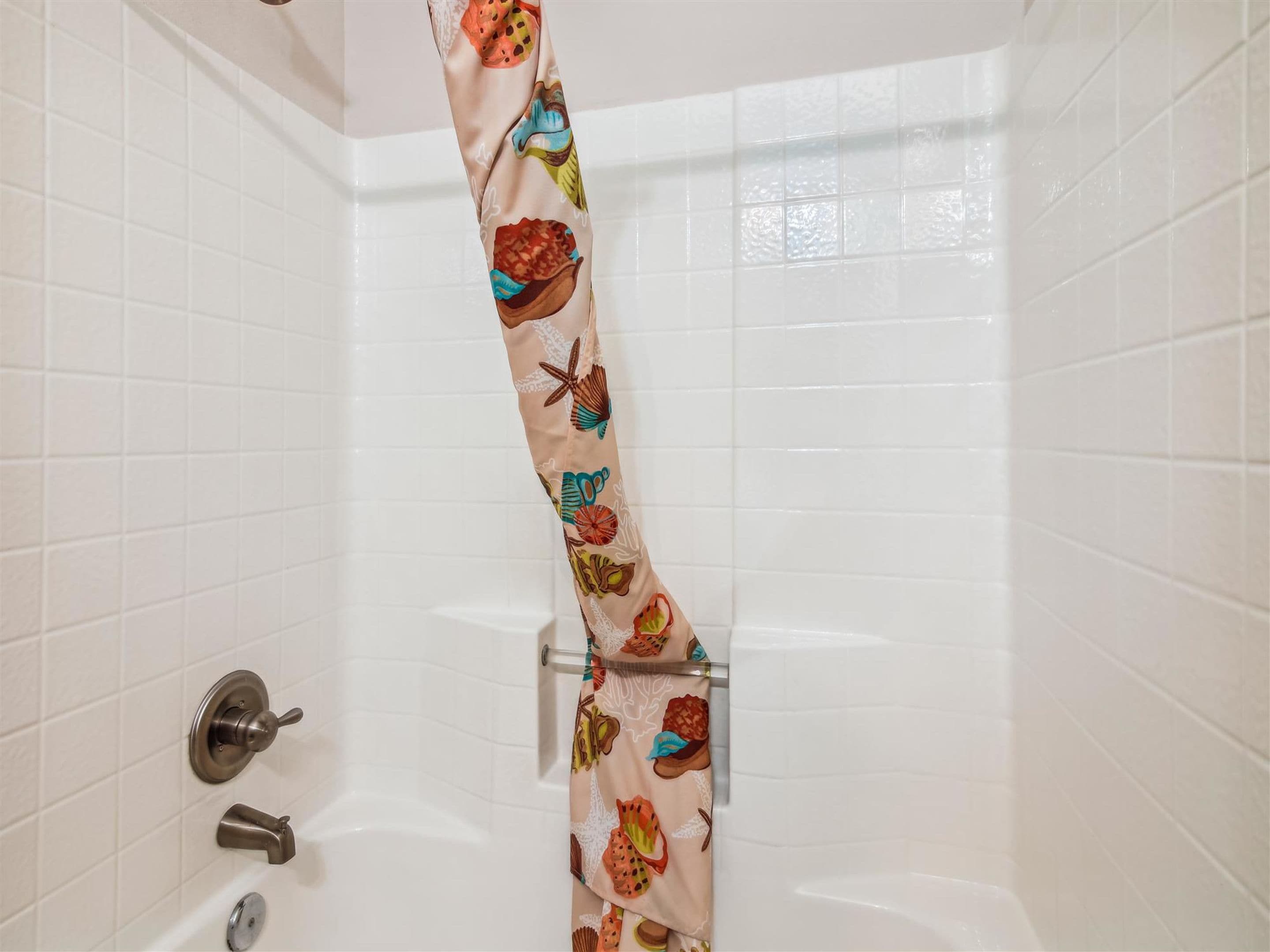 A bathroom with white tiled walls, a bathtub, a shower curtain with a colorful pattern, and a metallic faucet.