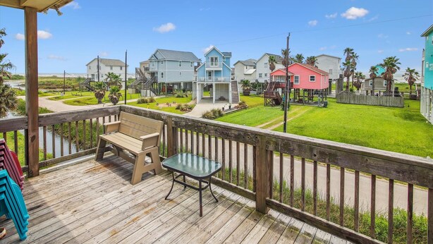 A wooden deck with a bench and table, overlooking a coastal neighborhood with colorful houses and a clear sky. - Sunny Beach Sandcastle Cottage by Ryson Vacation Rentals (Galveston)