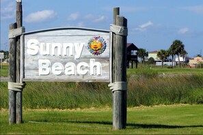 Un panneau en bois avec l’inscription « Sunny Beach » et un émoji représentant un soleil.