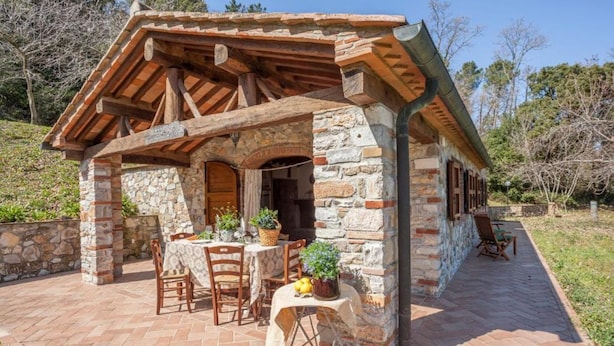 Una cabaña de piedra con techo de madera y un patio con mesas y sillas.