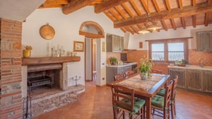 Una cocina rústica con vigas de madera a la vista, una chimenea de ladrillo y un comedor con mesa y sillas de madera.
