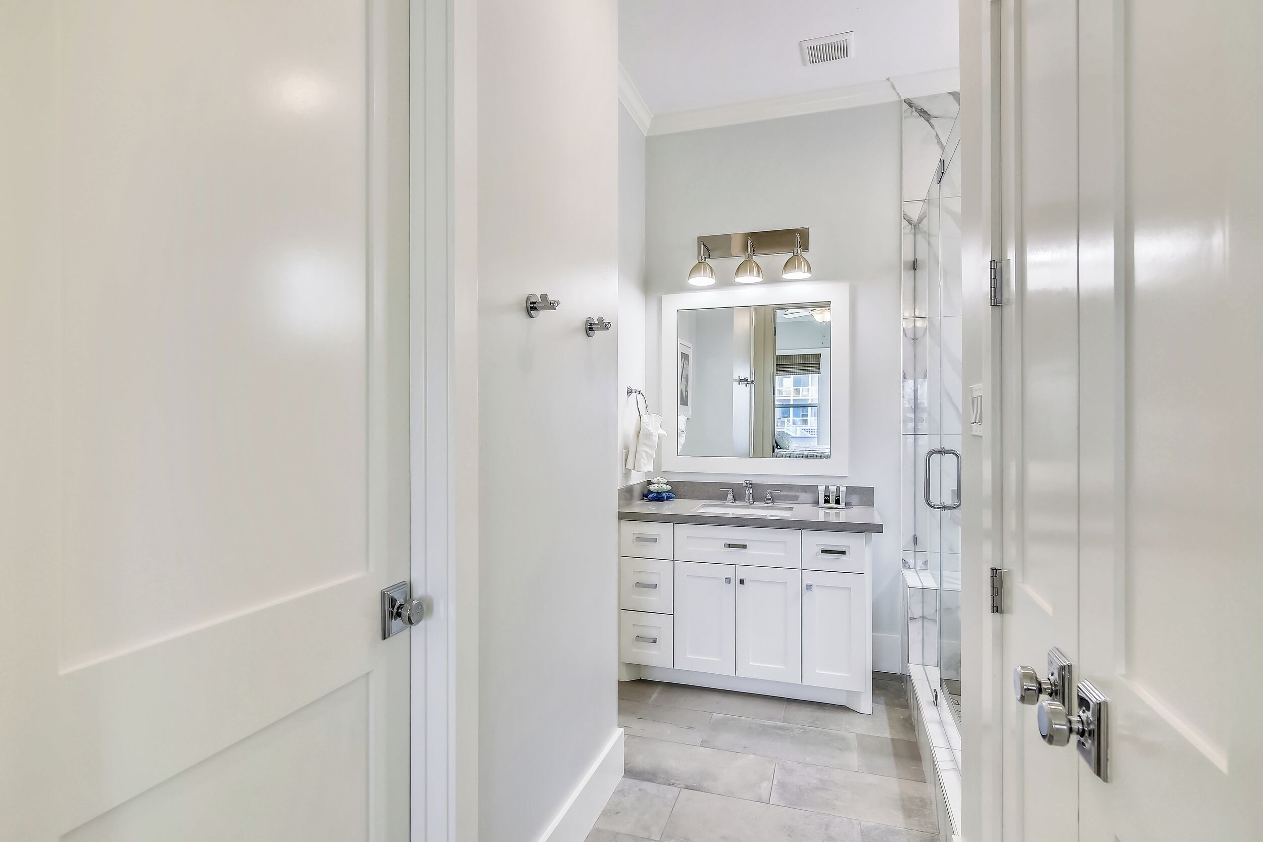 A modern bathroom with white cabinetry, a large mirror, and a shower area.