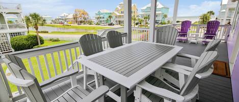 A covered outdoor seating area with a table and chairs, overlooking a residential area with houses and a body of water.