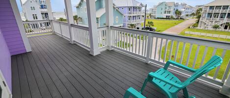 Um deck de madeira com cadeiras cor turquesa, com vista para uma área residencial com casas e gramado.