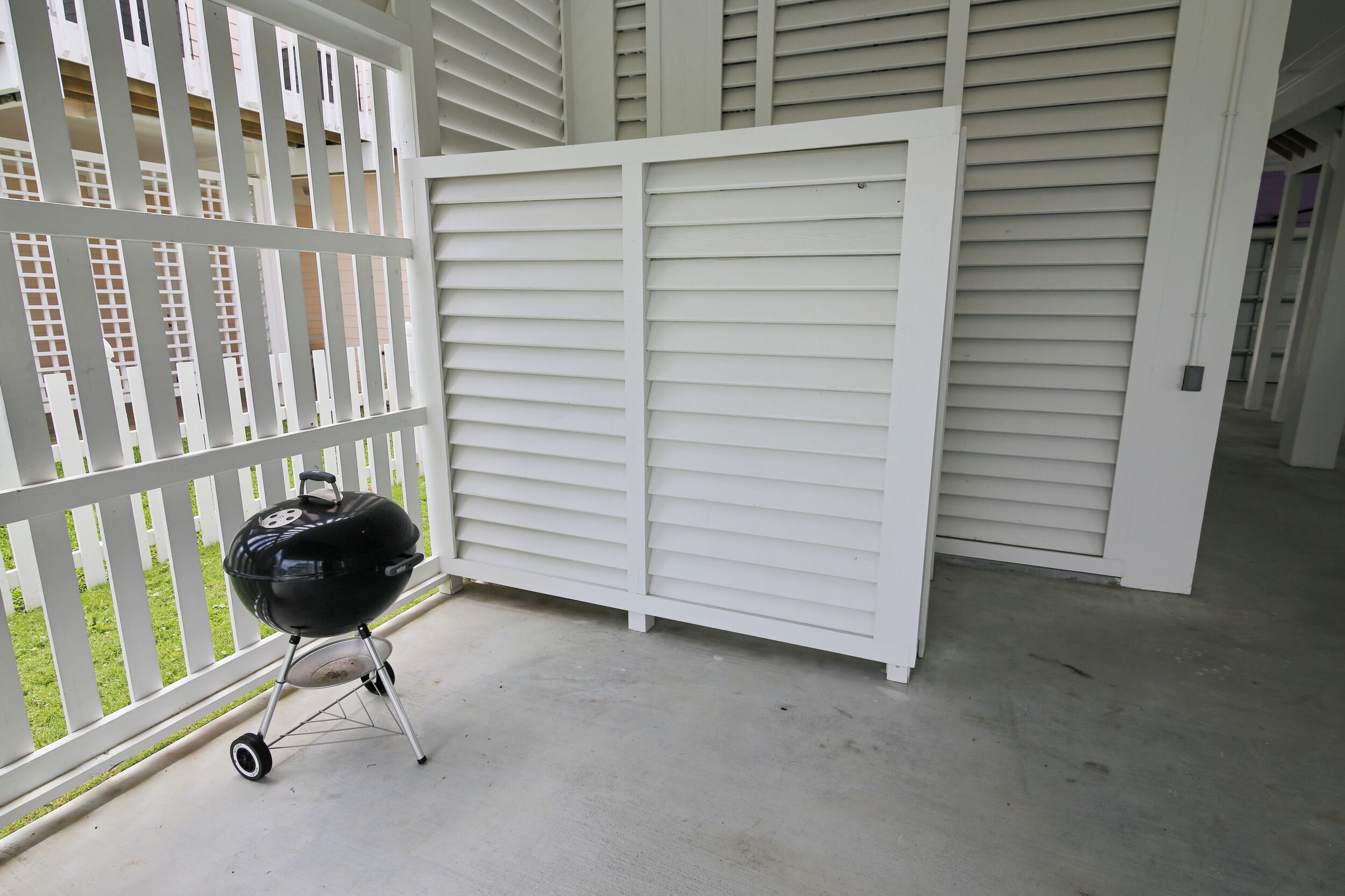 A balcony with a grill, white shutters, and a view of a building with windows.