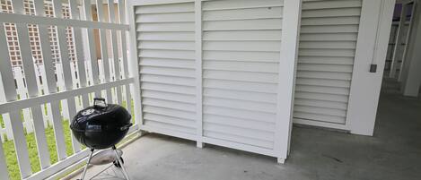 A balcony with a grill, white shutters, and a view of a building with windows.
