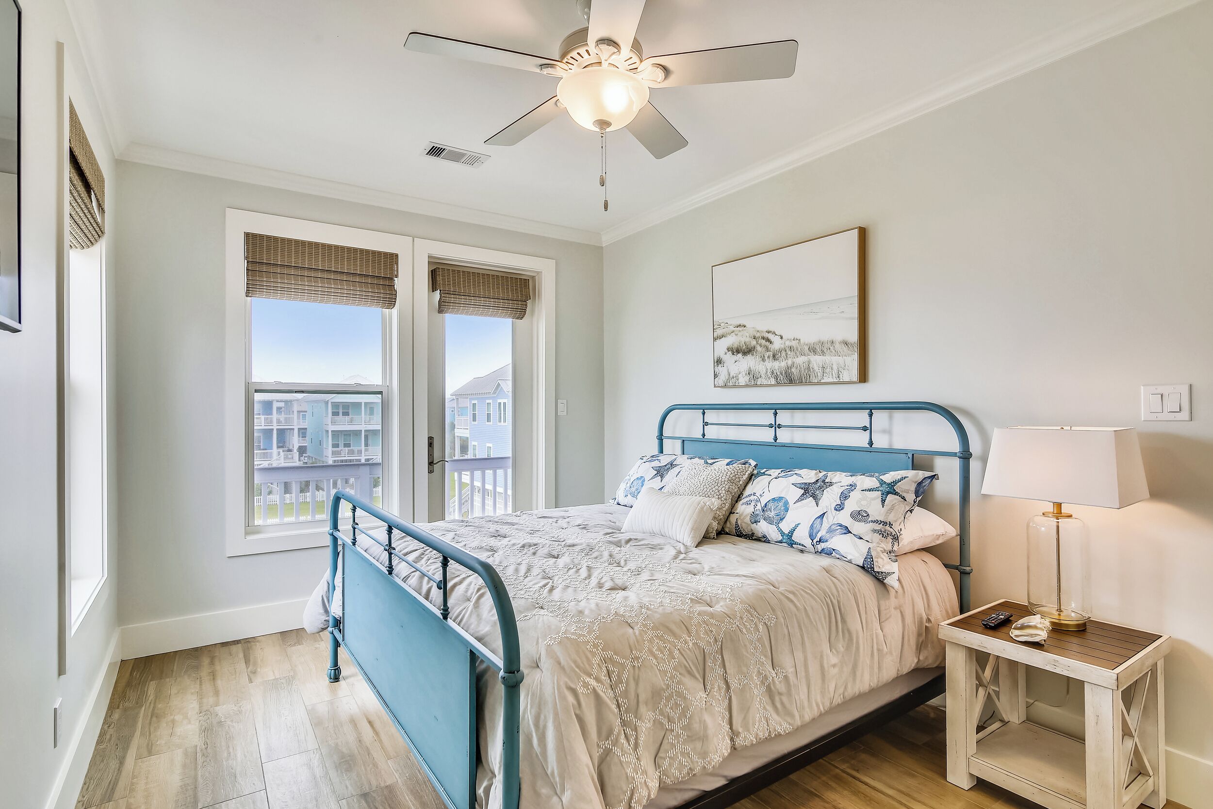 A bedroom with a bed, a nightstand, a ceiling fan, a window with blinds, and a painting on the wall.
