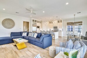 A modern living room with a sectional sofa, a yellow coffee table, and a dining area with a chandelier.
