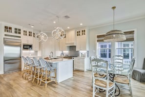 A modern kitchen with white cabinetry, a central island, and a dining area with wicker chairs.