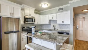 A kitchen with white cabinets, stainless steel appliances, a granite countertop, and a built-in oven. - Room with a View by Ryson Vacation Rentals (Galveston)