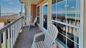 A balcony with two Adirondack chairs, a railing, and a view of the beach and ocean. - Room with a View by Ryson Vacation Rentals (Galveston)