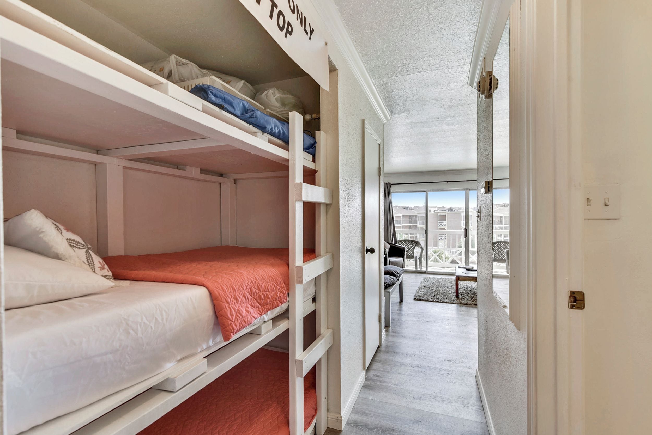 Une chambre avec des lits superposés, un panneau indiquant «Seulement le lit du haut», une porte donnant sur un balcon et une vue sur les bâtiments environnants.