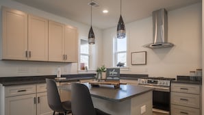 A modern kitchen with a central island, two bar stools, stainless steel appliances, and pendant lighting.