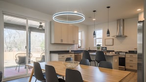 A modern kitchen with a dining area, large windows, and a view of the outdoors.