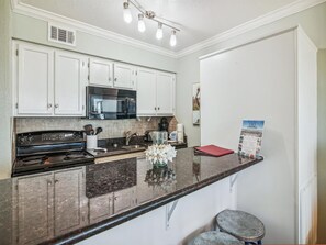 Kitchen features a black stove, microwave, and sink, with ample counter space and a light fixture above.