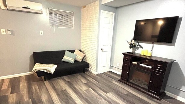 A living room with a black sofa, wooden flooring, a TV mounted on the wall, and a small cabinet.