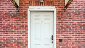 A white door with a small step leading up to it, set against a brick wall with a red and orange painted base.