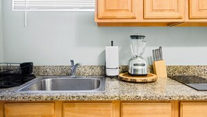 A kitchen with a granite countertop, stainless steel sink, wooden cabinets, a blender, and a knife block.