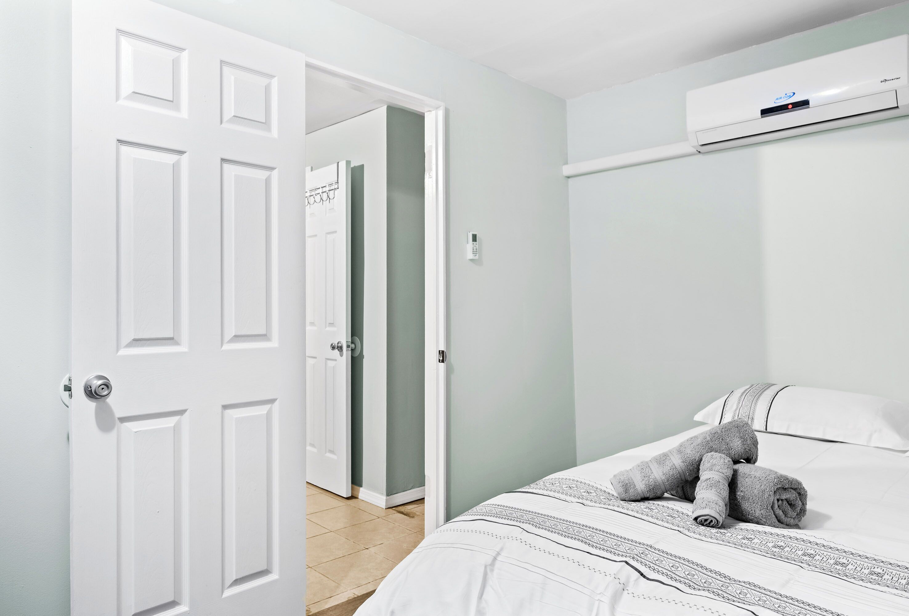 A bedroom with a bed, a white door, a wall-mounted air conditioner, and a hallway.